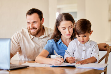 Obraz premium Writing, family and laptop for learning of child, mother and father with kid, watch and smile for education. Home, table and parents together with boy, knowledge and video for school and weekend