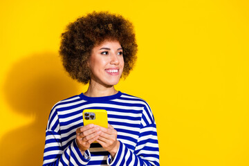 Photo of nice young girl hold phone look empty space wear striped shirt isolated on yellow color...