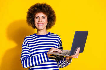 Portrait of smart positive girl with perming coiffure dressed striped pullover holding laptop smile...