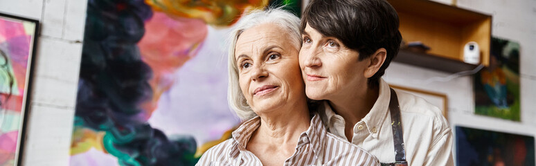 Two women admire paintings in art studio.