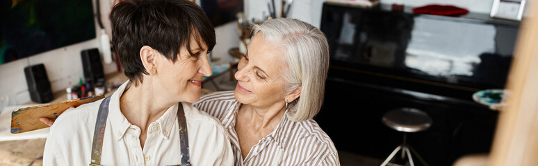 Mature lesbian couple standing together in art studio.