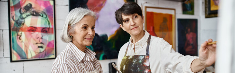 Two women admire paintings in a gallery room.
