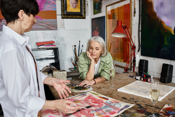 A mature lesbian couple admires a piece of art in a studio.