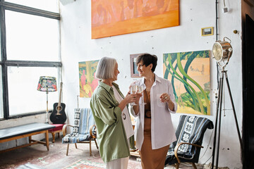 Mature lesbian couple standing in art studio.