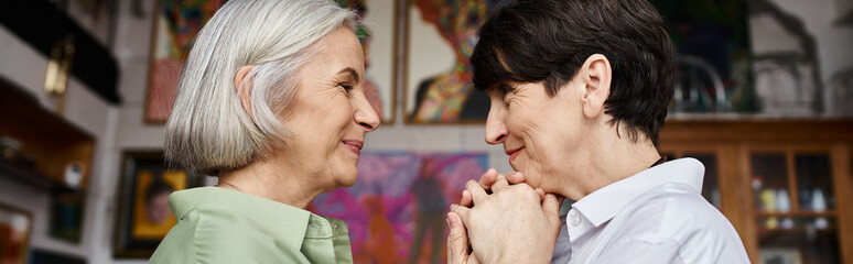 Mature lesbian couple stands together in art studio.