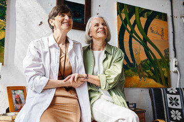 A mature lesbian couple peacefully sitting next to each other in an art studio.