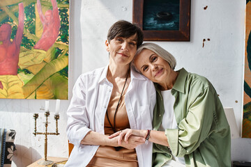 Two mature lesbian women, serenely sitting together in an art studio.
