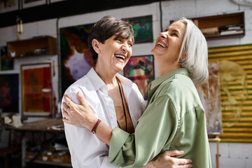 A mature lesbian couple hugging tenderly in an art studio.