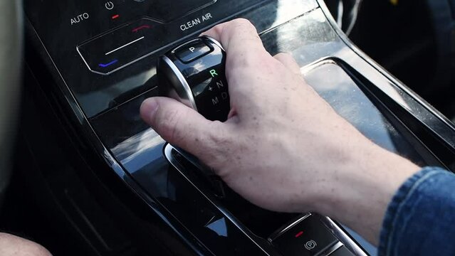 The gearshift knob of the automatic transmission of a modern automobile. Man's hand shifts speeds of automatic transmission.