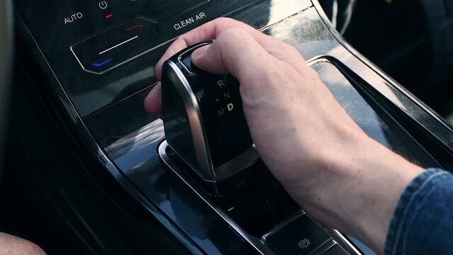 The gearshift knob of the automatic transmission of a modern automobile. Man's hand shifts speeds of automatic transmission.