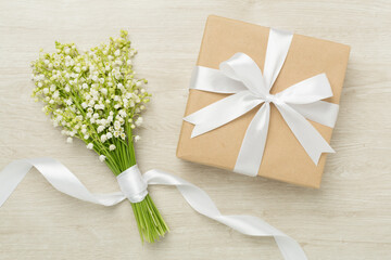 Lilies of the valley with gift box on wooden background, top view