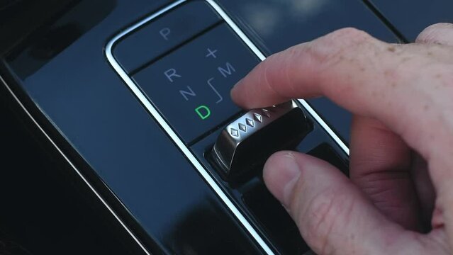 Minimalist gearshift knob of the automatic transmission of a modern automobile. Man's hand shifts speeds of automatic transmission.