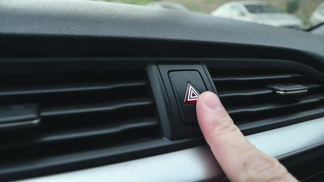 Person turns on a car's hazard warning flasher button, close-up.