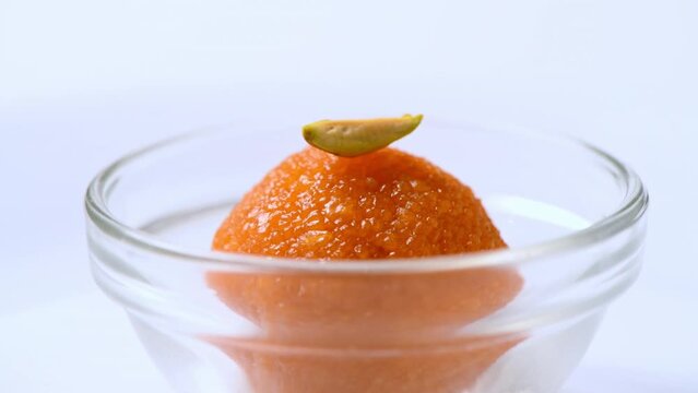 Delicious looking Motichur ladoo (motichoor) in a glass bowl. Closeup front shot of motichur laddoo rotating slowly against white . Yummy looking indian sweet . Ladoo with pistachio topping.
