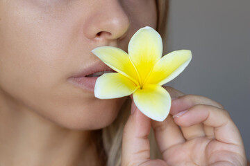Cropped shot of a young caucasian woman holding and sniffing a white and yellow frangipani flower...