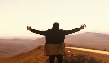A man looks on the hills with hands wide open. Happy hiker enjoys sunny day