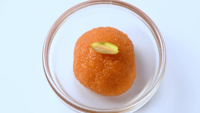 Delicious looking Motichur ladoo (motichoor) in a glass bowl. Closeup top shot of motichur laddoo rotating slowly against white . Yummy looking indian sweet . Ladoo with pistachio topping.