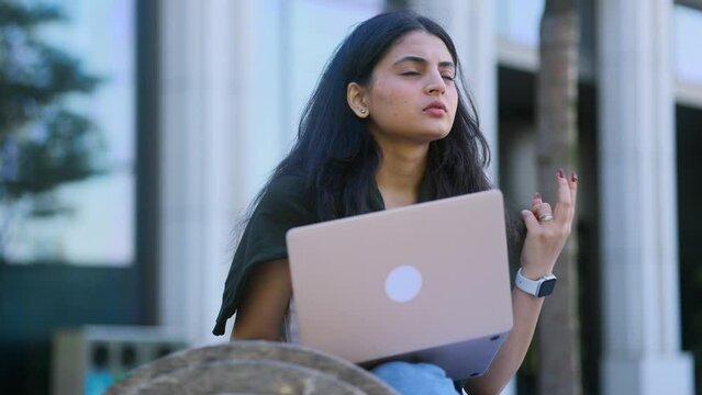 Portrait of beautiful young indian woman thinks questioningly about difficult choice choose imagine plan in mind has doubts create idea with laptop computer at city centre	