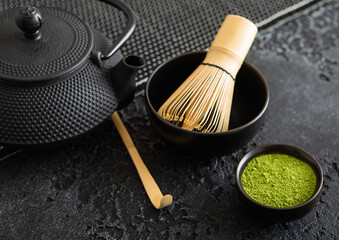 Green matcha tea with bamboo spoon and whis and japanese iron cast kettle on black background.