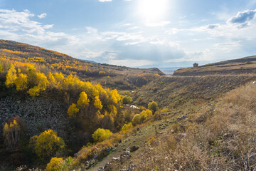 Autumn landscape of a canyon, trees with yellow leaves and hillocks. Ruins of a church at the top