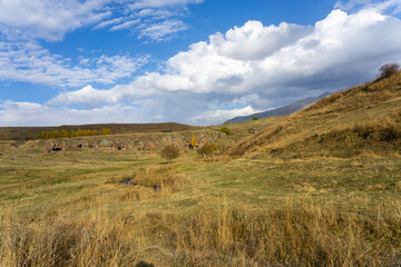 Obraz premium Autumn landscape of rocks, hillocks and mountains. Green grass, bright sky with clouds