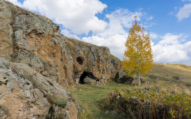 Birch tree with yellow leaves near a church carved into the rock. Samsari