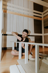 A young man manually drives a screw into a hole in the side of a bunk bed ladder.