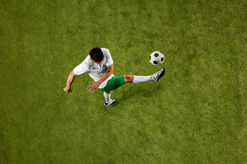 Aerial view. Dynamic shot of young athletic man, wearing comfortable jersey and shorts posing to make perfect pass. Concept of professionals sport, competition, tournament, energy, action. Ad
