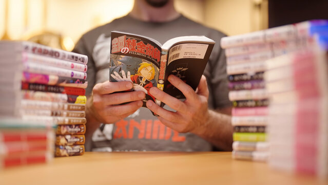 Headless person reading Japanese manga comic Fullmetal Alchemist among the pile of light novels and manga