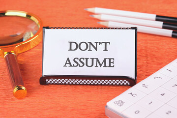 Don't assume text concept on a white business card in a stand with a magnifying glass, pencils and...