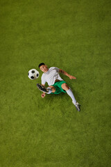 Overhead view of young fit guy, footballer in motion, perfectly positioned to strike ball on green grass field. Concept of professionals sport, competition, tournament, energy, action. Ad