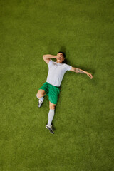 Defeat moment. High-angle shot of athlete in white shirt and green shorts, lying on grass with his hands shielding his face. Concept of professionals sport, competition, tournament, energy, action. Ad