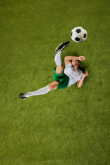 Dynamic top-down photo of footballer in green and white gear, captured in mid-air while attempting...