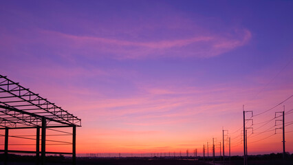 Colorful twilight sky background over silhouette row of electric poles with part of warehouse...