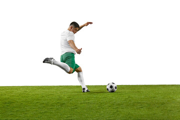 Side view of young fit man, soccer player ready to kick a soccer ball on green grass field against...