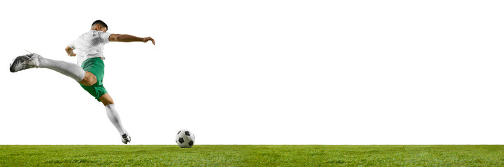 Banner. Young fit man, soccer player ready to kick a soccer ball on green grass field against white...