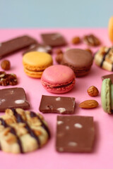 Pastel macarons, almond chocolate, peanut butter cookies and various nuts on bright pink background. Selective focus.