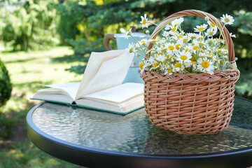 Composition with  basket of chamomile flowers, book on table. Good morning concept. Side view. Space for text.	