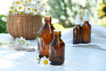 Bottles of chamomile essential oil or infusion, bunch of chamomile and bowl of daisy flowers on background. Alternative herbal medicine. Side view. 