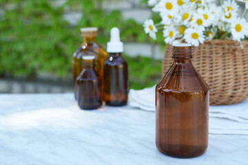 Glass bottle of chamomile essential oil with fresh chamomile flowers in basket. Healthy ingredient. Alternative medicine and herbal therapy concept. Side view. Space for text.