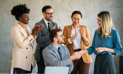 Multiethnic business people shaking hands while their colleagues applauding and smiling in office