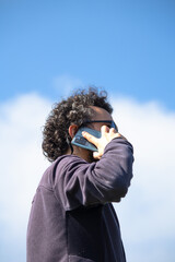 Fototapeta premium Turkish Man talking on mobile phone on blue sky background. Curly haired man with smartphone. 