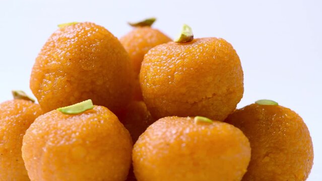 Delicious looking Motichur ladoos (motichoor) stacked up on a plate. Closeup shot of motichur laddoos rotating slowly against white . Yummy looking indian sweets . Ladoos with pistachio topping.