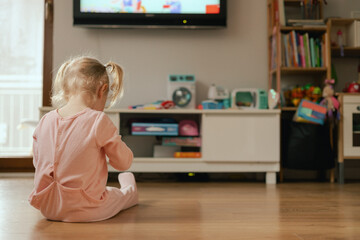 Portrait of happy baby playing with toys and watches cartoons on TV in playroom. Children and...