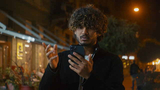 Lost Indian Arabian Latino American man walk city center night using mobile phone cellphone help online maps app gps technology alone outside uncertainty route misunderstanding location confused male 