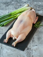 Whole Raw Duck with Head and Feet on Unlit Black Plate