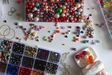 Colorful beads, letter beads, threads and other jewelry making supplies on white background. Making friendship bracelets concept. Flat lay.