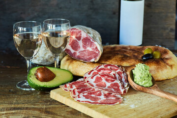Dried sausage. On the background there are two glasses of white wine, a bottle, bread and avocado.