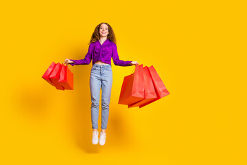 Full length photo of lovely young lady jump hold shopping bags dressed stylish violet garment isolated on yellow color background