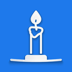 Paper cut Burning candle in candlestick icon isolated on blue background. Cylindrical candle stick with burning flame. Paper art style. Vector